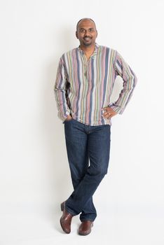 Full length confident Indian guy in casual wear standing on plain background with shadow.