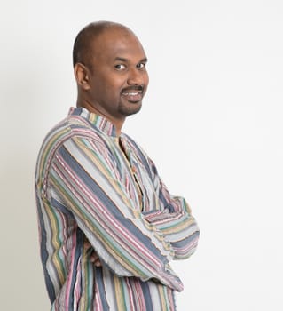 Portrait of smiling Indian man arms crossed looking at camera on plain background with shadow