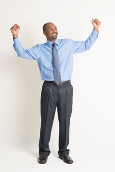 Full body Indian businessman hand celebrate and looking up at blank copy space, standing on plain background with shadow