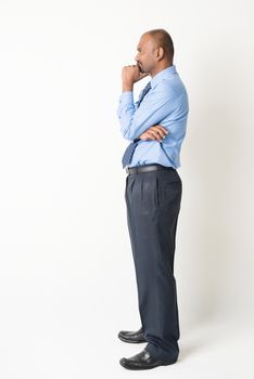 Profile view of full body Indian businessman hand on chin looking at blank copy space, standing on plain background with shadow