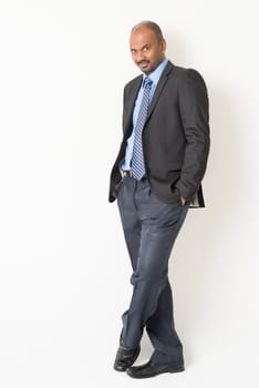 Full length cool Indian businessman in formal suit looking at camera, on plain background.