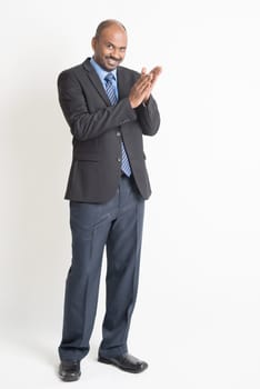 Full length happy Indian businessman in formal suit clapping hands and looking at camera, on plain background.