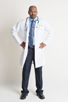 Full length Indian male medical doctor in uniform standing on plain background with shadow. 