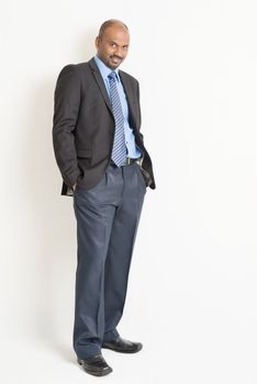 Full length Indian businessman in formal suit looking at camera, on plain background.