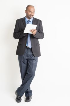 Full body Asian Indian businessman using digital tablet pc standing over plain background