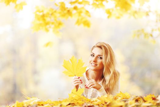 Happy young woman laying on autumn leaves in park