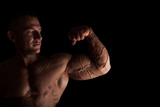 Handsome bodybuilder showing big biceps isolated on black background. Health fitness.