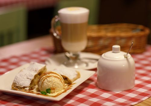 Fragrant coffee latte in glass cup and and strudel with ice cream on a tablecloth in a cage