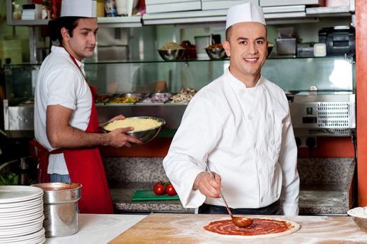 Male chef preparing the pizza base with sauce