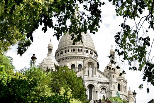 View of the "Sacre Coeur" in Paris through a frame of leaves and trees in the lush garden.