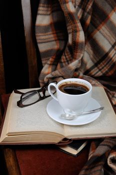 A cup of coffee on a chair with a stack of books and a blanket