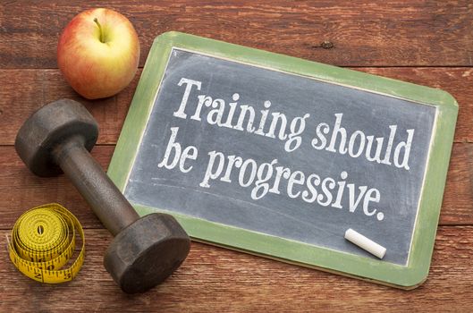 training should be progressive -  slate blackboard sign against weathered red painted barn wood with a dumbbell, apple and tape measure