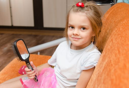 Five year old girl sitting on the couch with a mirror in her hand