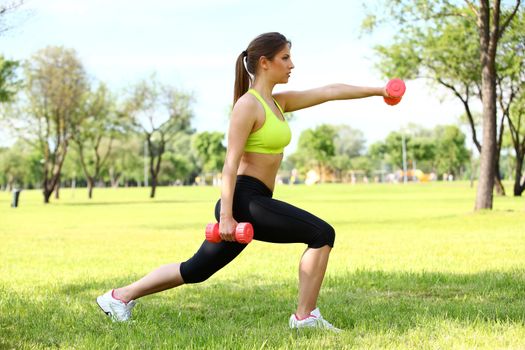 Beautiful young caucasian woman working out with dumbbells in the park