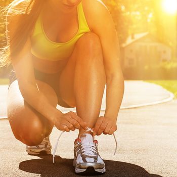 Beautiful young woman in fitness wear ties shoelaces outdoors