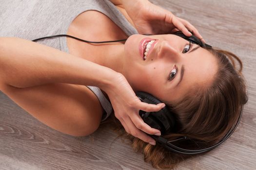 Beautiful caucasian woman listening music with headphones lying on the wooden floor