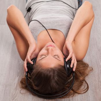 Beautiful caucasian woman listening music with headphones lying on the wooden floor