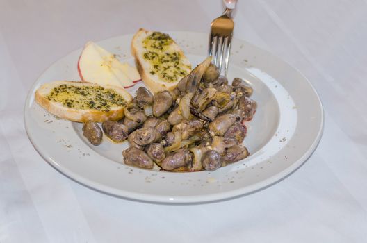 Piquant fried chicken hearts with onions and garlic bread against white background.