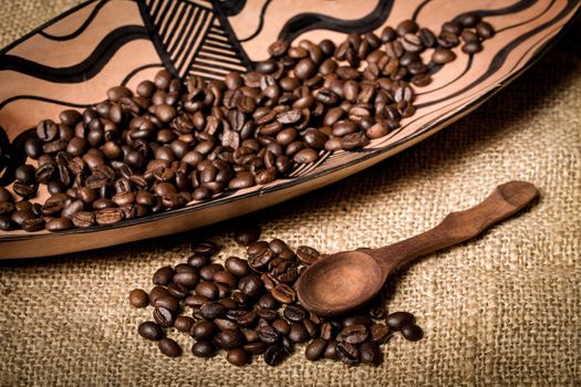 pile of fresh and bio aromatic coffee beans in african bowl and wooden spoon