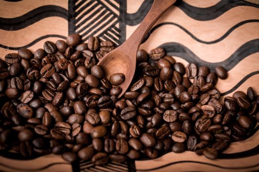 pile of fresh and bio aromatic coffee beans in african bowl and wooden spoon