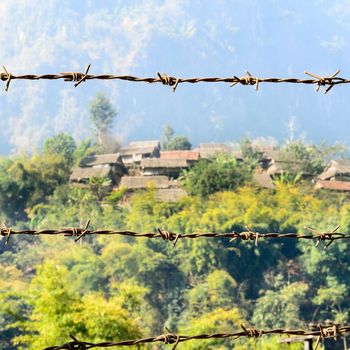 The Barbed Wire in front of Refugee House that made from Wood,Bamboo and Leaf Roof at Refugee Camps in the North of Thailand.