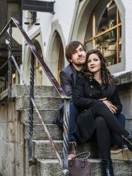 Photo of a young couple sitting and resting in an old town in Europe.
