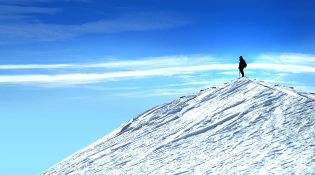 Climber on top of the mountain contemplating nature  Man on the mountain top with snow and blue sky.