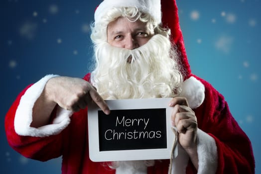 Santa Claus pointing a finger on a blank slate with text Merry Christmas