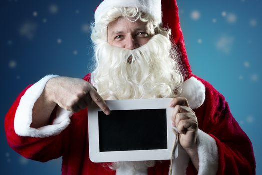 Image portrait of Santa Claus in red coat with snow pointing a finger on a blank slate