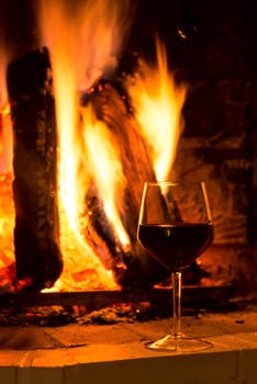 Glass of red vine near burning fireplace