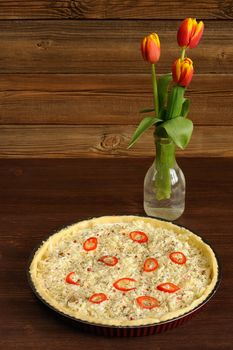 Red and yellow tulips and open cheese pie with chili on wooden background with space