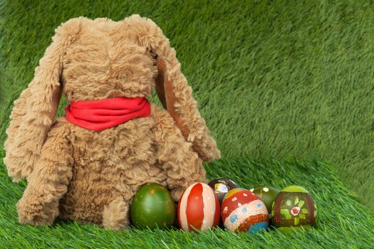 Rabbit, sit on green grass and group of colorful eggs are behind, can use as background for happy easter festival