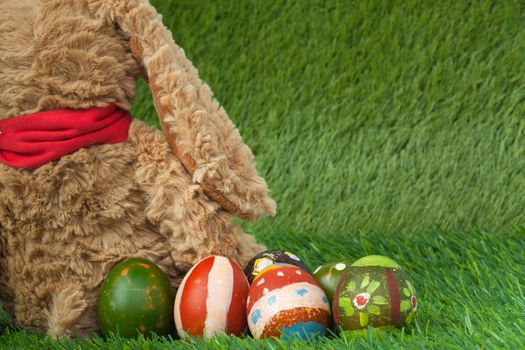 Rabbit, sit on green grass and group of colorful eggs are behind, can use as background for happy easter festival