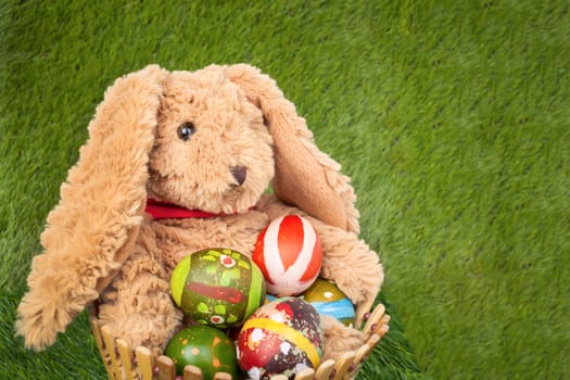 Rabbit, sit and holding colorful eggs in basket on grass for happy easter festival