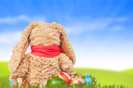 Rabbit, sit on green grass and group of colorful eggs are behind with blue sky background for happy easter festival