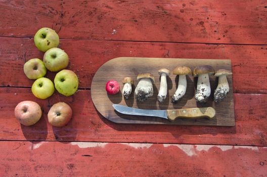kitchen cutting board with mushrooms and apples on red wooden table