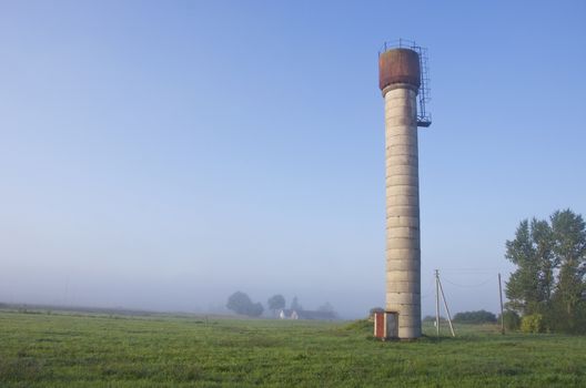 rural early morning landscape with water tower and mist fog