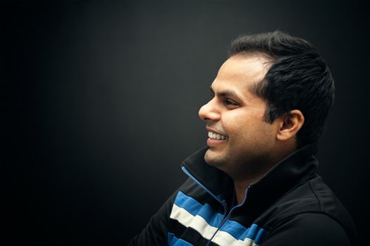 Portrait of Indian man smiling over dark background wearing jacket