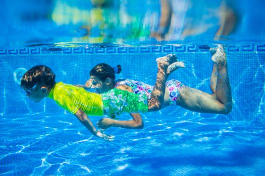 Underwater happy cute girl and boy in swimming pool