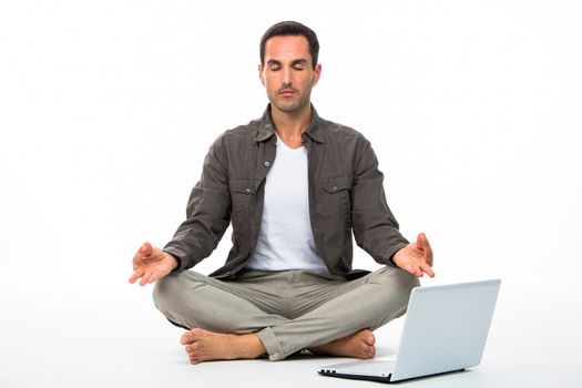 Man sitted on the floor with eyes closed practicing yoga with laptop next to him