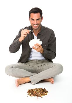 Man sitted on the floor, smiling at camera, holding a coin to be placed in a piggy bank