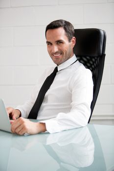 Half length portrait of male businessman, smiling at camera and working with a laptop computer
