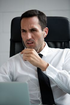 Half length portrait of a angry male businessman with earphones and laptop computer