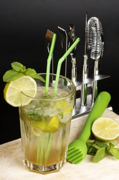 Mojito cocktail with two straws, lime slice and spearmint leaves, some of it's ingredients and a cocktail set