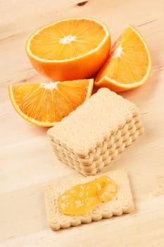 Some biscuits, marmalade, and a cut orange over a wooden table. Everything is ready for an healthy breakfast.