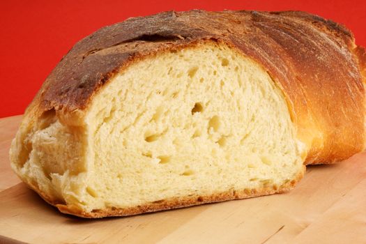 Freshly baked bread from Apulia on a wooden cutting board over a red background.