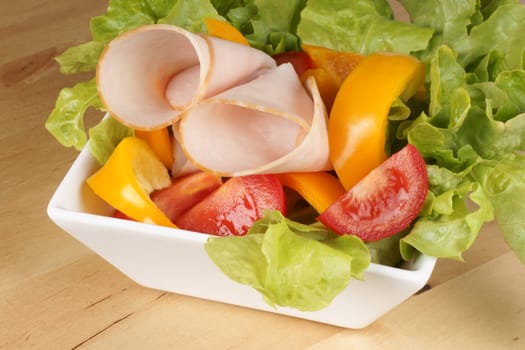 Close-up of a mixed salad with lettuce, tomatoes, bell peppers and roast turkey over a wooden cutting board