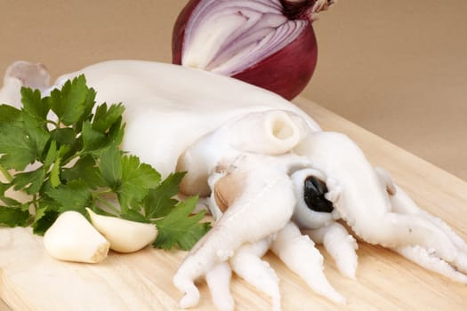 Raw cuttlefish on a wooden cutting board with red onion, parsley and garlic.