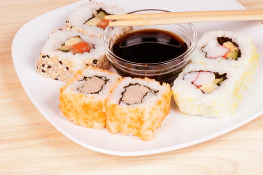Close-up of Maki sushi rolls served on a plate with soy sauce and chopstick on a wooden table