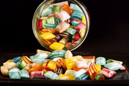 Colorful hard candies in a glass jar and on a black tray over a black background